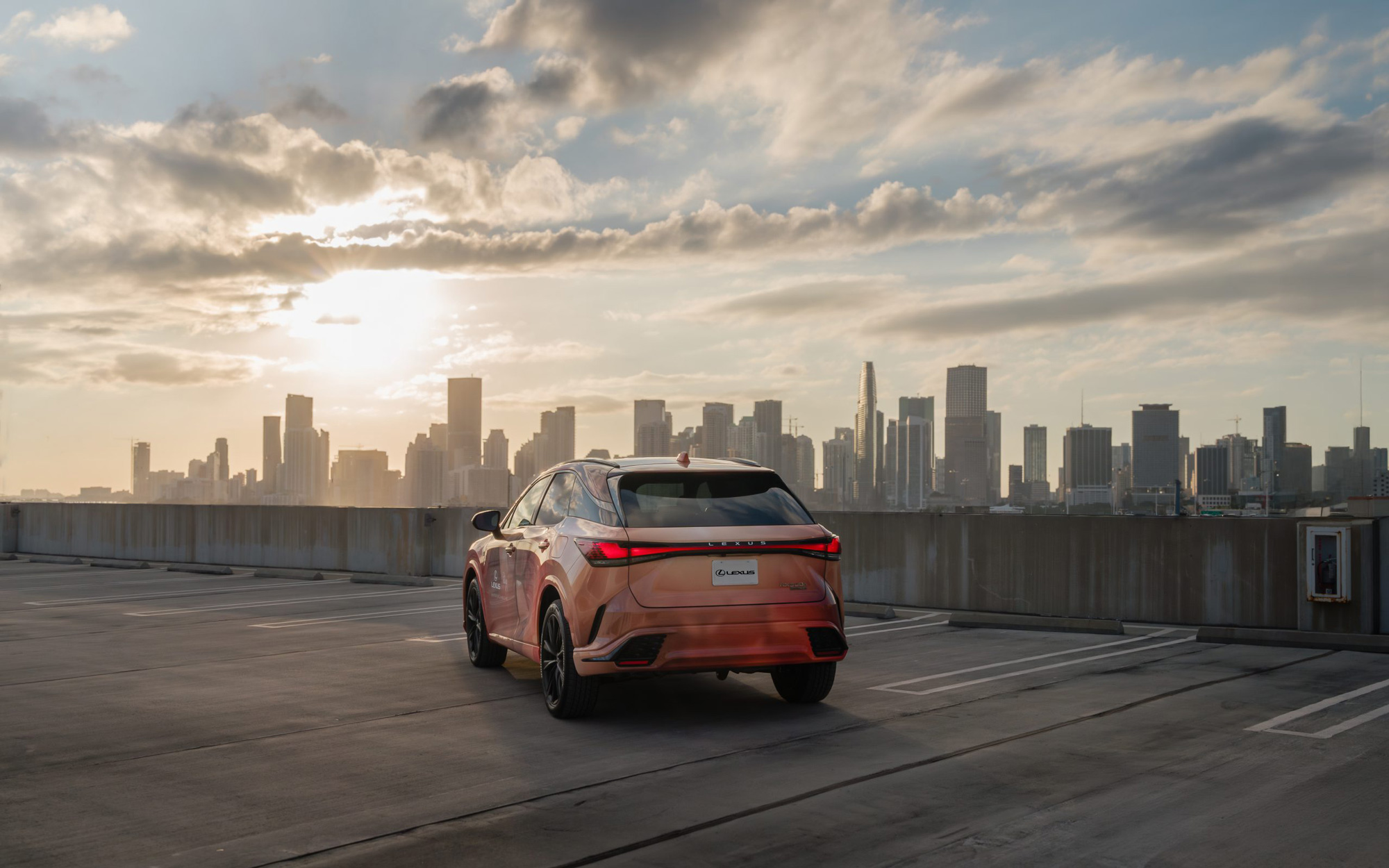 Orange Lexus RX on top of a Miami parking garage rooftop, enhanced with high-end retouching that highlights the vehicle’s luxurious lines and urban backdrop. Photographed by Konrad Langer, edited by Janine Langer, Graphic Designer from Berlin.